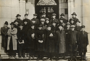 Students graduating from the Faculty of Law in 1921.  Most students are wearing the school uniform. Some students wear a felt hat or hunting cap, rather than the round cap.